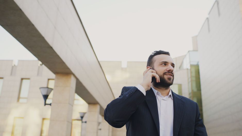 Empresário confiante conversando no smartphone do lado de fora de um prédio moderno.