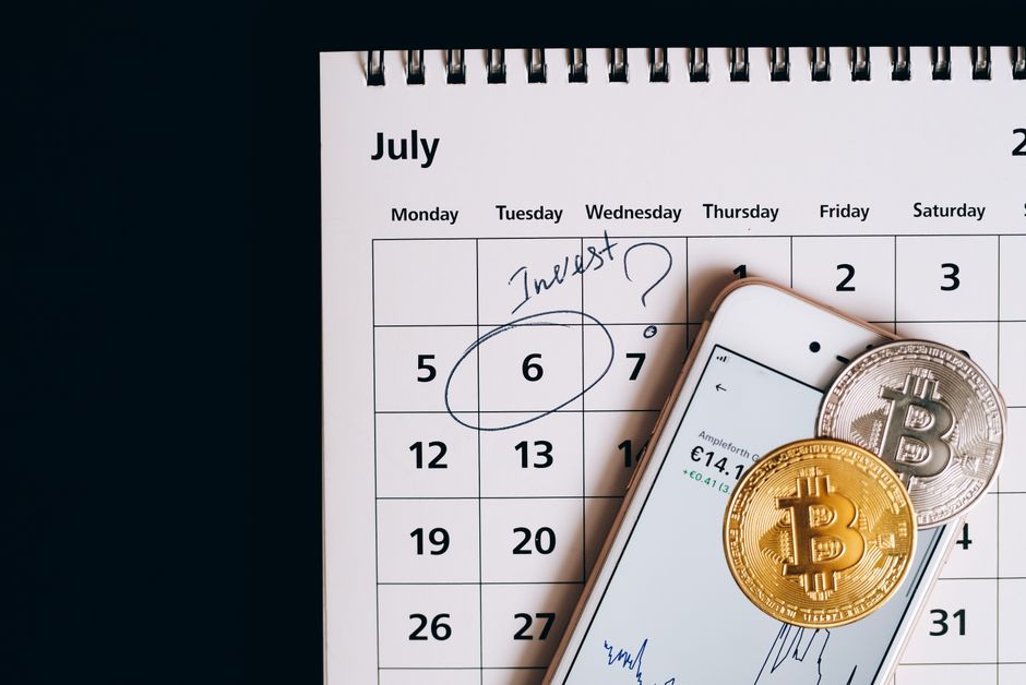 Smartphone com bitcoins em calendário, marcando a data do investimento.