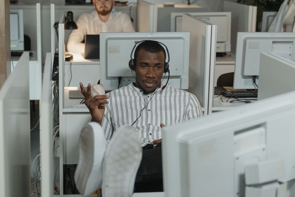 Homem relaxando em cubículo de escritório, usando fones de ouvido e segurando uma bola antiestresse.
