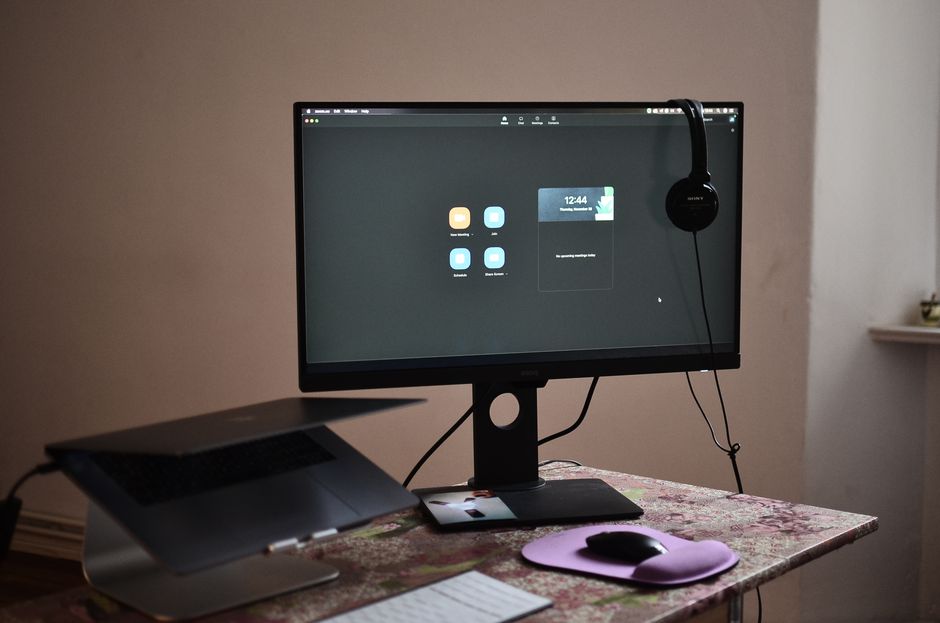 Configuração moderna de mesa de escritório em casa com um monitor de computador e laptop, ideal para trabalho remoto e videoconferências.
